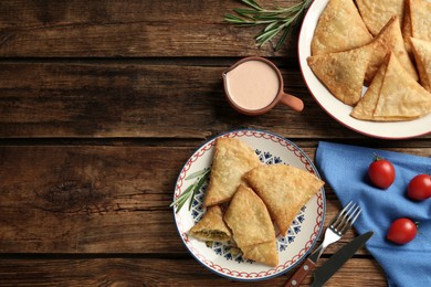 Photo of Delicious samosas with sauce on wooden table, flat lay. Space for text