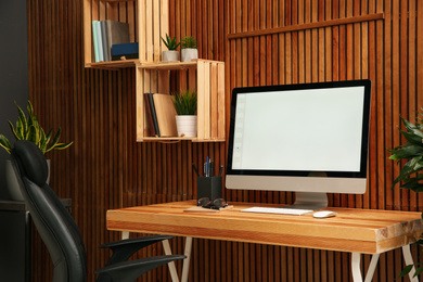 Comfortable workplace with computer near wooden wall in stylish room interior. Home office design