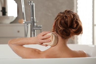 Woman with sponge taking bath indoors, back view