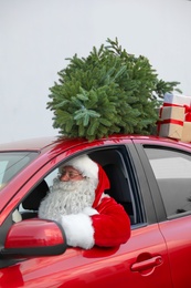 Authentic Santa Claus driving red car with gift boxes and Christmas tree, view from outside