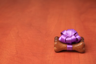 Photo of Bone shaped dog cookies with purple bow on wooden background, space for text