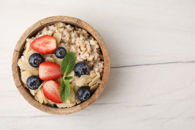 Photo of Tasty oatmeal with strawberries, blueberries and almond petals in bowl on white wooden table, top view. Space for text