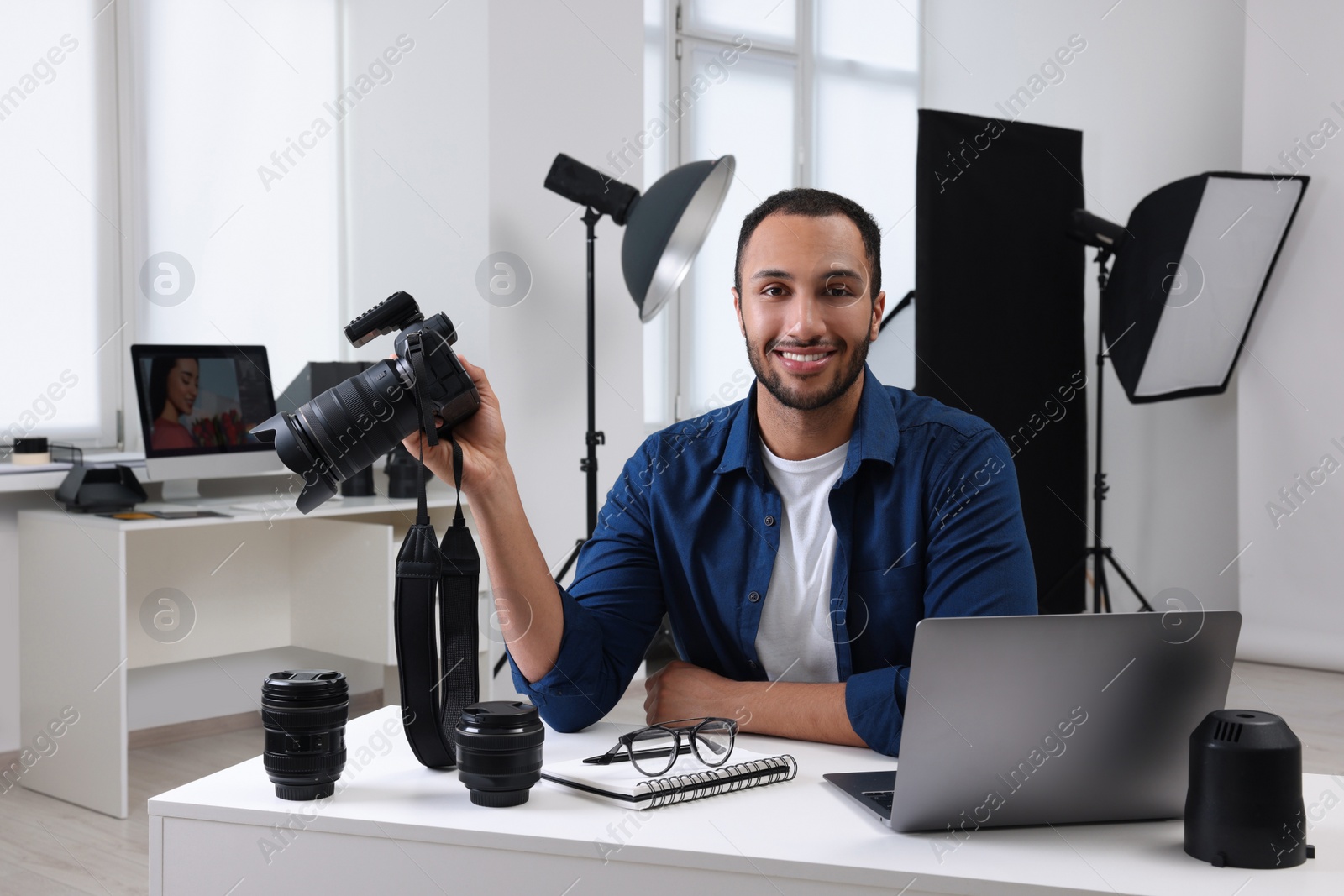 Photo of Young professional photographer with camera at table in modern photo studio