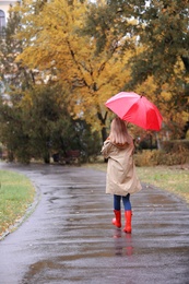 Woman with umbrella taking walk in autumn park on rainy day