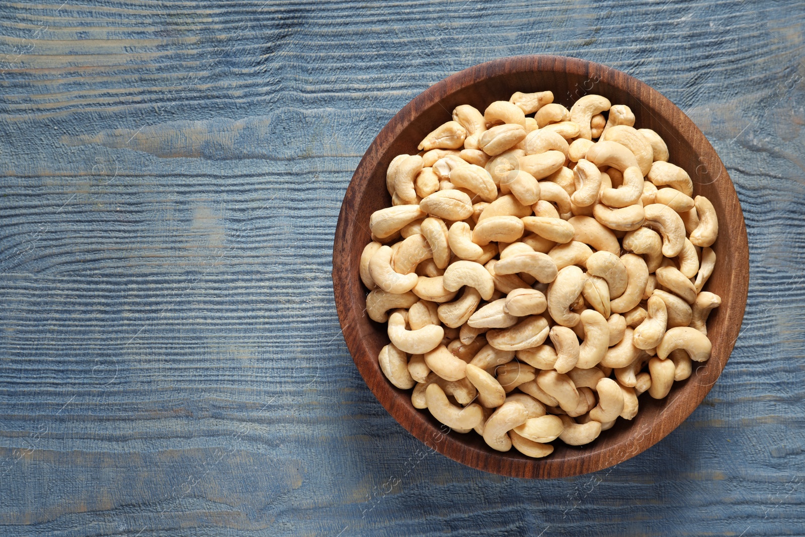 Photo of Tasty cashew nuts in bowl on wooden table, top view. Space for text