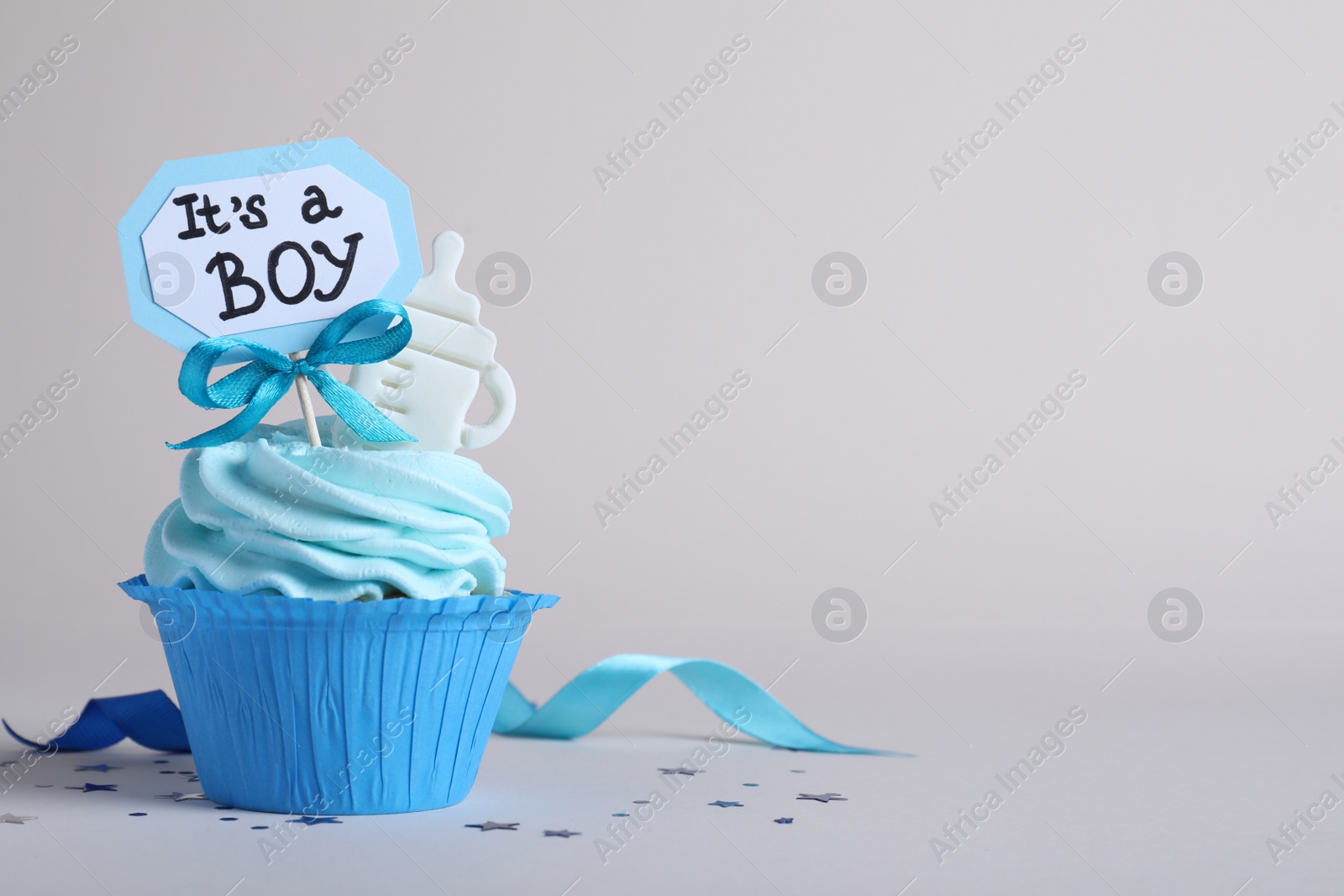 Photo of Beautifully decorated baby shower cupcake with cream and boy topper on light grey background. Space for text