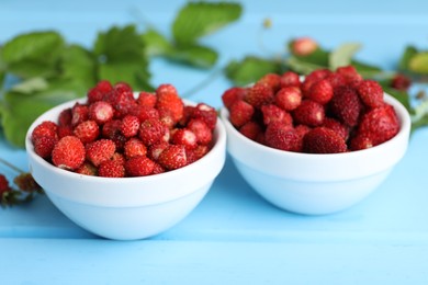 Photo of Fresh wild strawberries in bowls on light blue table