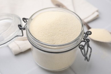 Photo of Uncooked organic semolina in jar on white tiled table, closeup