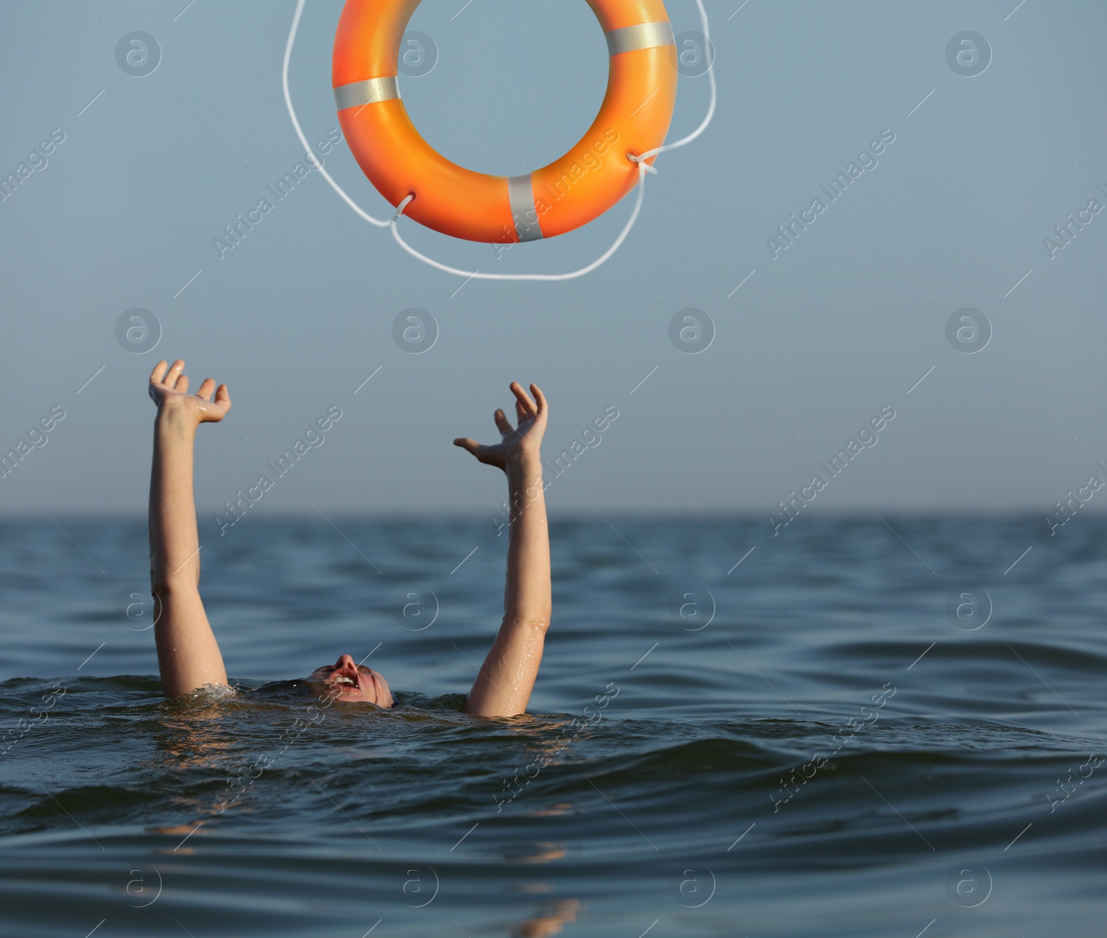 Image of Drowning woman with raised hands getting lifebelt in sea