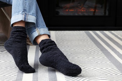 Photo of Woman in warm socks relaxing near fireplace at home, closeup