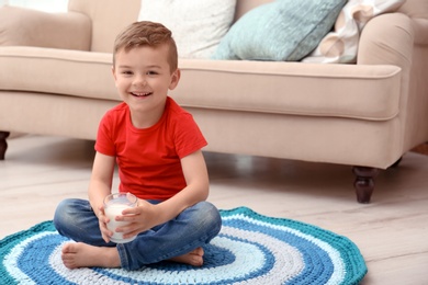 Photo of Cute little boy with glass of milk on floor at home