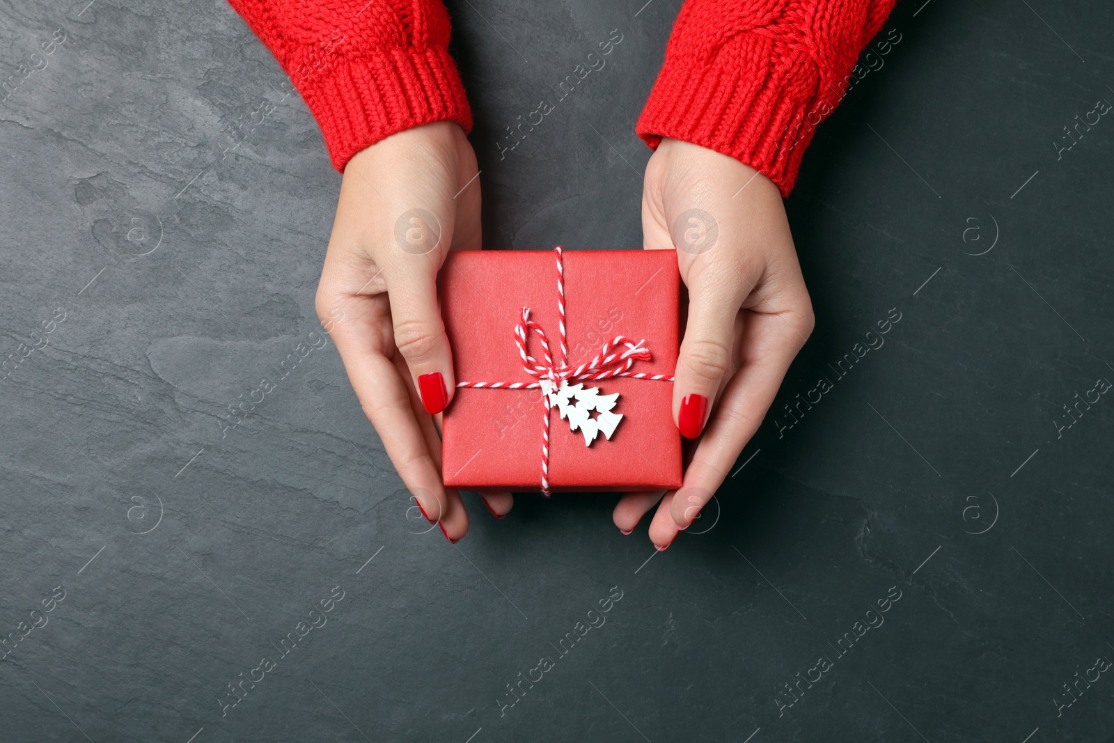 Photo of Christmas present. Woman with gift box at black table, top view