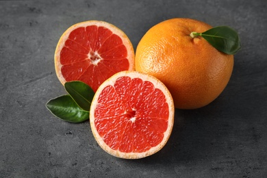 Photo of Fresh tasty grapefruits with leaves on grey table