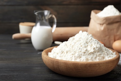 Photo of Bowl with flour on wooden table