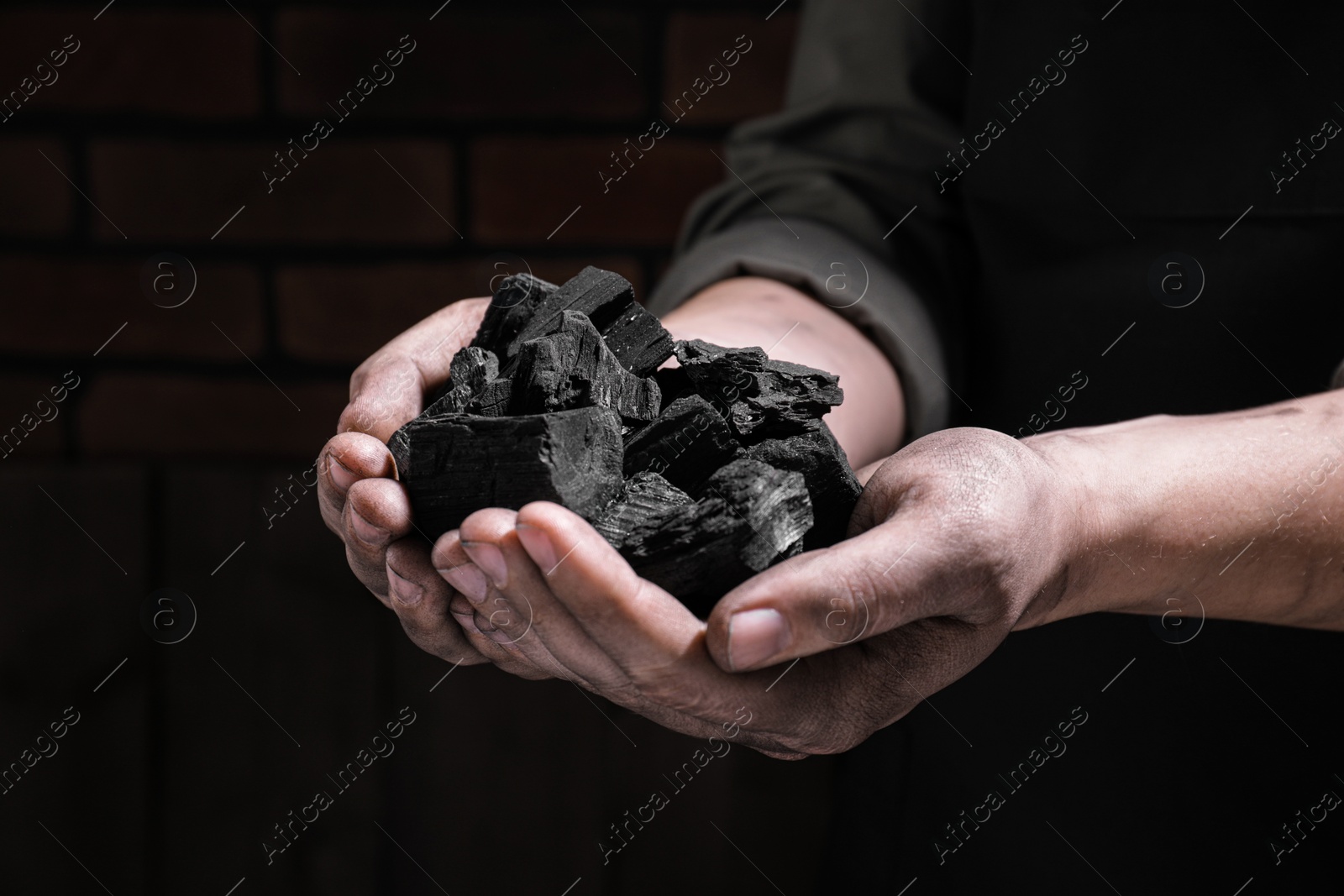 Photo of Man with handful of coal near brick wall, closeup view