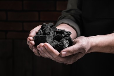 Man with handful of coal near brick wall, closeup view