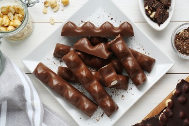 Photo of Tasty chocolate bars with nuts on white wooden table, flat lay