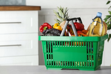 Photo of Shopping basket with grocery products on grey table indoors. Space for text