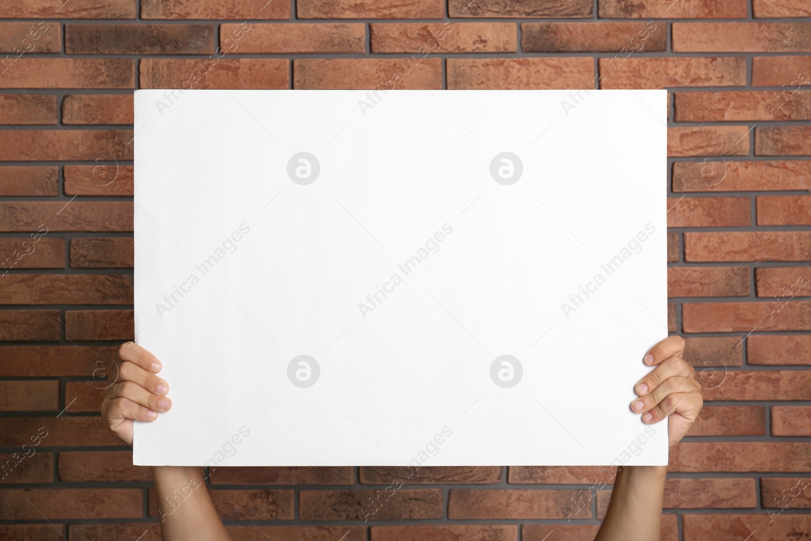 Photo of Man holding white blank poster near red brick wall, closeup. Mockup for design