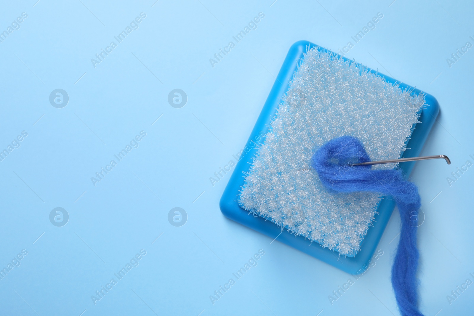 Photo of Brush, felting wool and needle on light blue background, top view. Space for text