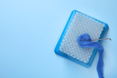 Photo of Brush, felting wool and needle on light blue background, top view. Space for text