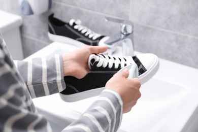 Photo of Woman washing stylish sneakers with brush in sink, closeup