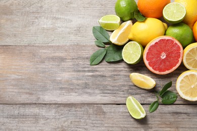 Photo of Different fresh citrus fruits and leaves on wooden table, flat lay. Space for text