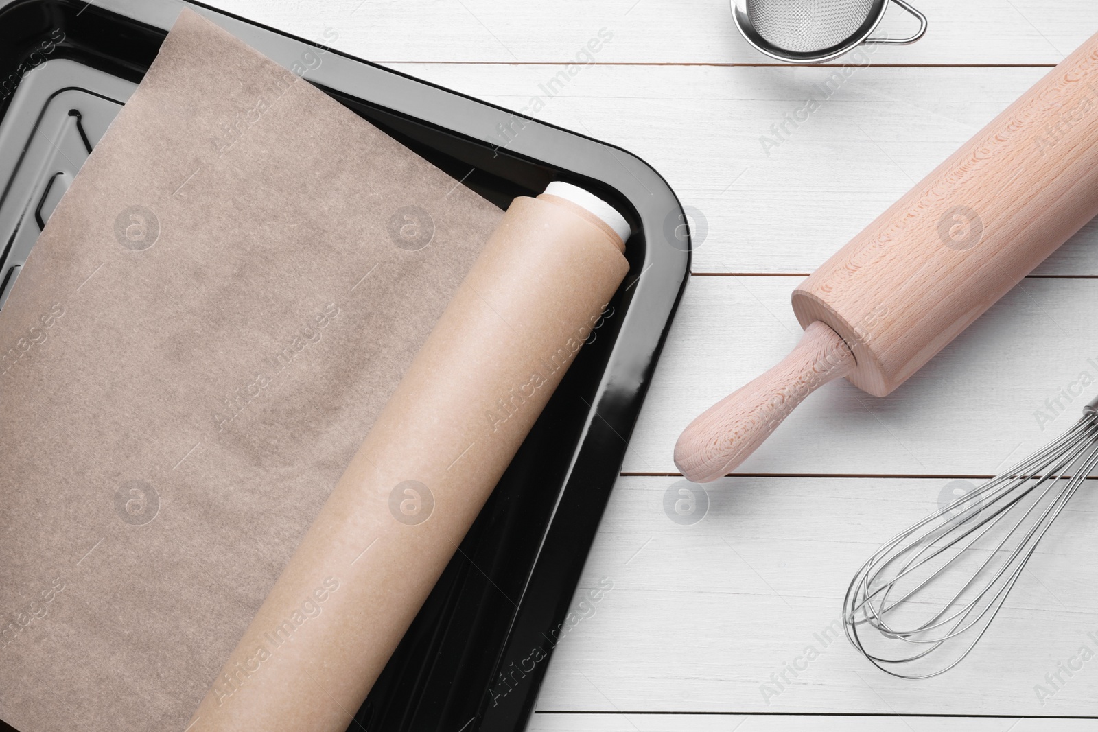 Photo of Baking pan with parchment paper and kitchen utensils on white wooden table, flat lay