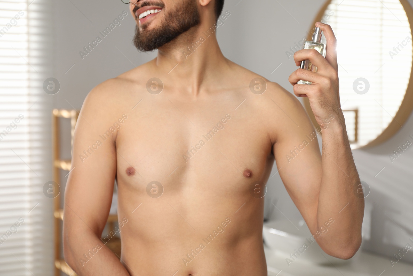 Photo of Young man spraying luxury perfume indoors, closeup