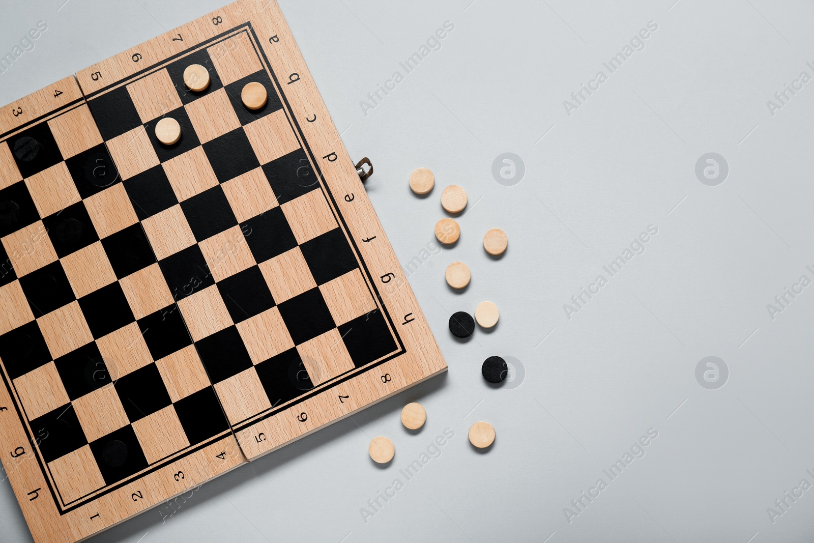 Photo of Wooden checkerboard and game pieces on light grey background, flat lay. Space for text