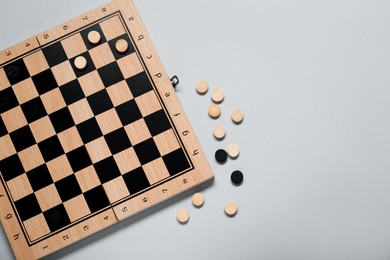 Photo of Wooden checkerboard and game pieces on light grey background, flat lay. Space for text