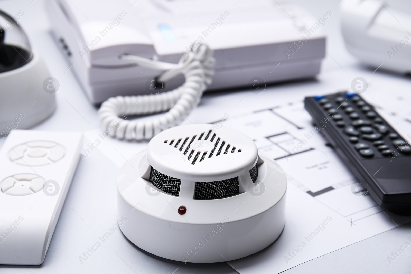 Photo of Smoke detector, remote controls and building plan on white background, closeup. Home security system