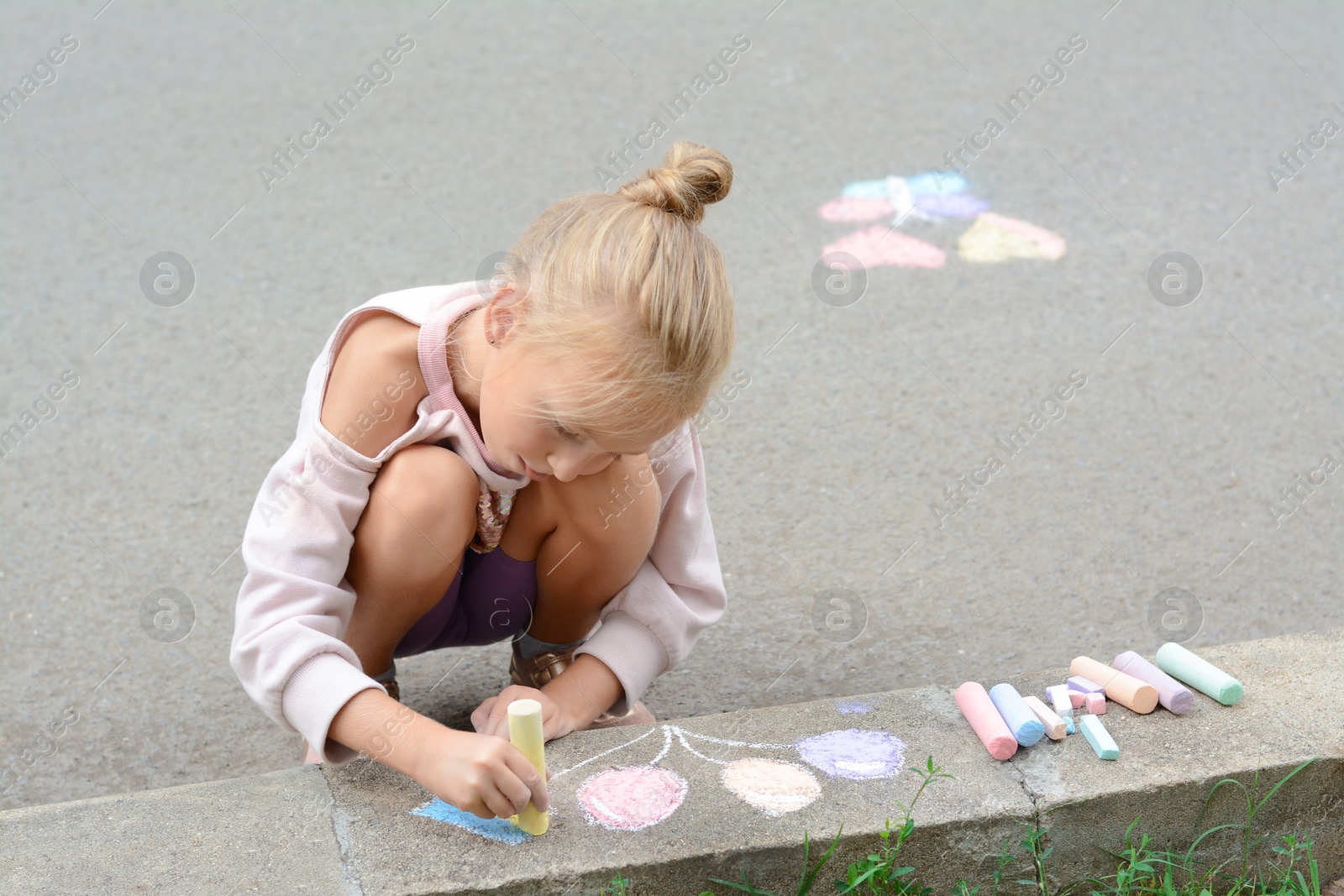 Photo of Little child drawing balloons and ukrainian flag with chalk on curb outdoors, space for text