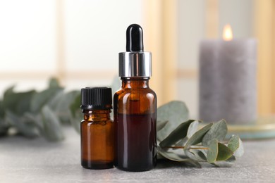 Aromatherapy. Bottles of essential oil and eucalyptus leaves on grey table