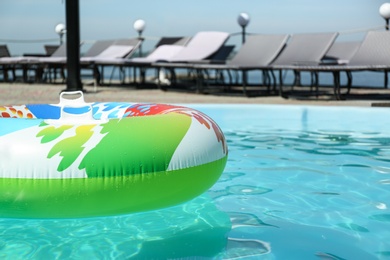 Colorful inflatable ring floating in swimming pool on sunny day, outdoors. Space for text
