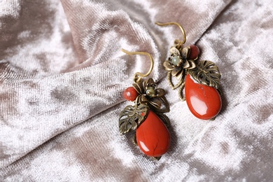 Photo of Beautiful pair of metal earrings with red jasper gemstones on light fabric, above view