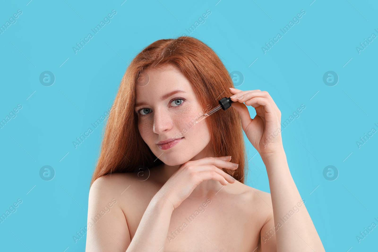 Photo of Beautiful woman with freckles applying cosmetic serum onto her face against light blue background