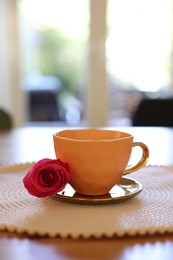 Cup of hot drink and red rose on table indoors