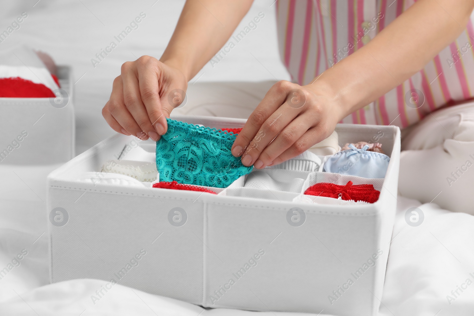 Photo of Woman putting underwear into organizer on bed, closeup