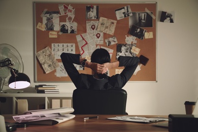 Detective looking at evidence board in office, back view