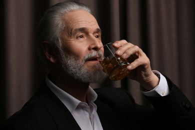 Photo of Senior man in suit drinking whiskey on brown background