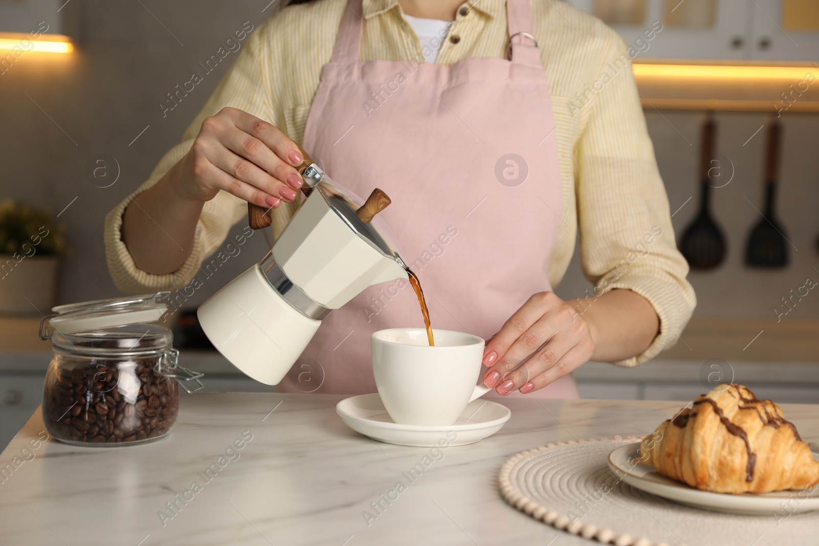 Photo of Woman pouring aromatic coffee from moka pot into cup at white marble table, closeup