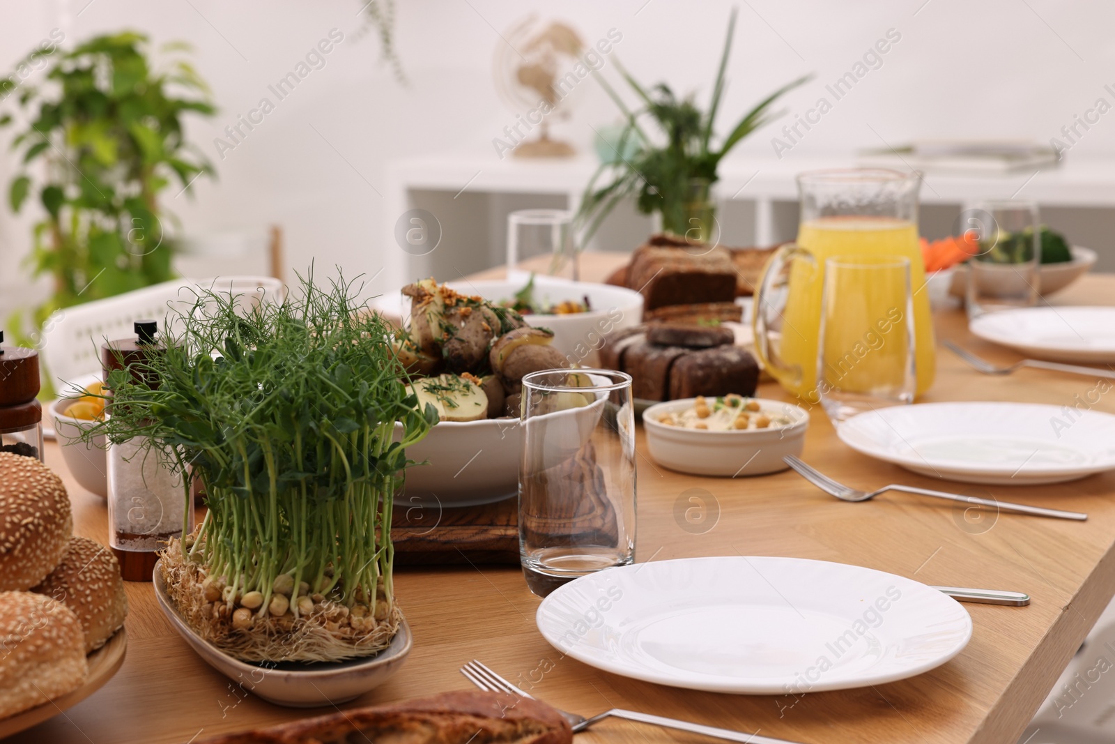 Photo of Healthy vegetarian food, jug of juice, cutlery, glasses and plates on wooden table indoors