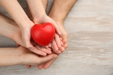 Photo of Top view of parents and kid holding red heart in hands at wooden table, space for text. Family day