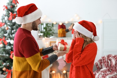 Photo of Young couple in Santa hats with Christmas gift at home