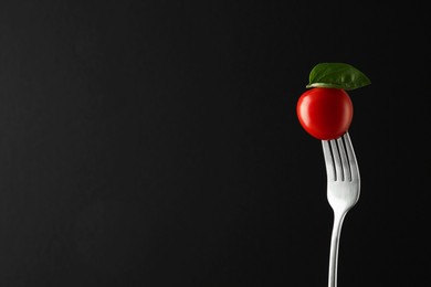 Photo of Fork with cherry tomato and basil on black background, space for text