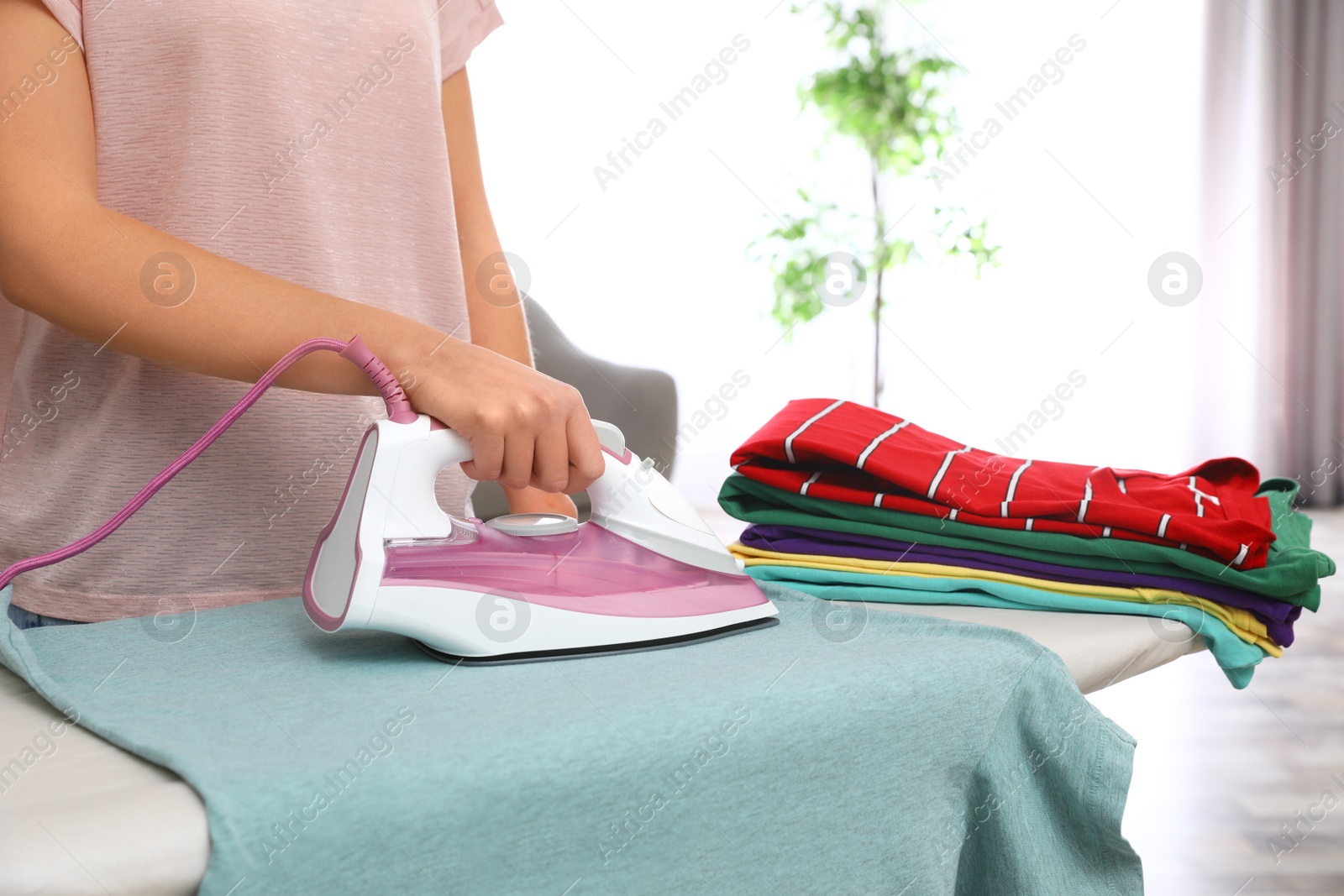 Photo of Young woman ironing clothes on board at home, closeup