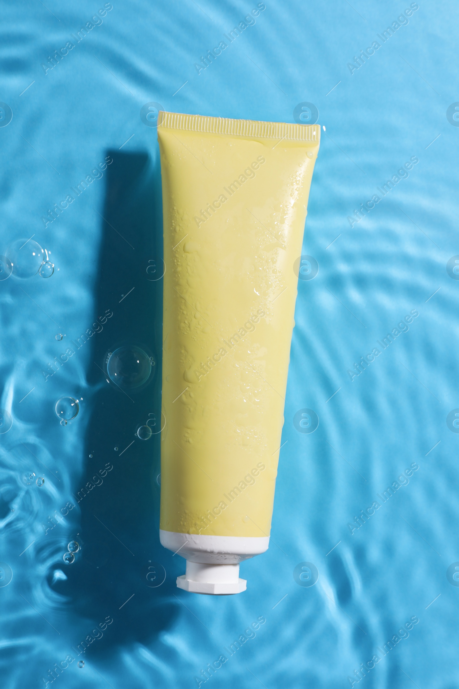 Photo of Tube with moisturizing cream in water on light blue background, top view