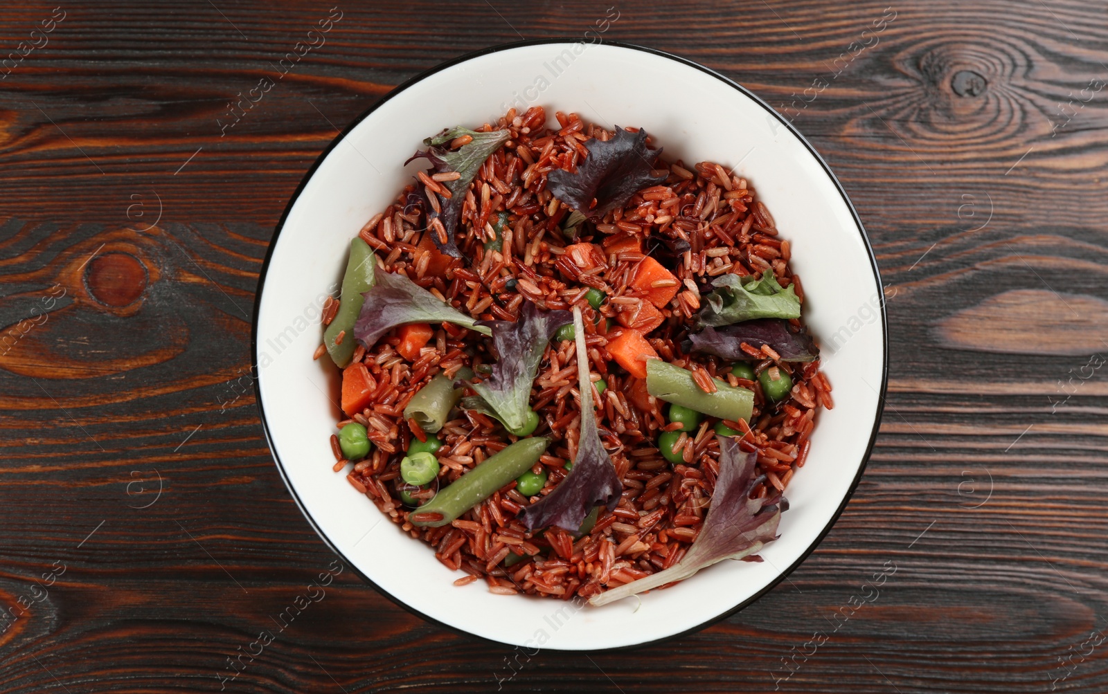 Photo of Tasty brown rice with vegetables on wooden table, top view