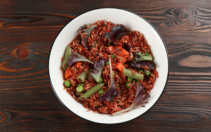 Photo of Tasty brown rice with vegetables on wooden table, top view